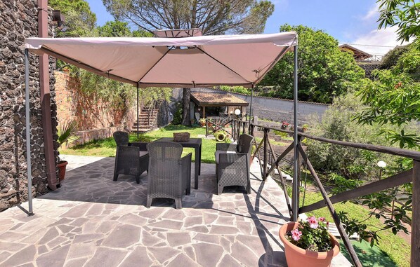 Eine Terrasse im Freien mit Steinboden, Korbmöbeln und einem großen Sonnensegel.