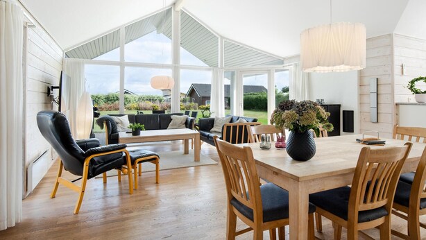 A spacious room with a large dining table, wooden chairs, a sofa, and a TV mounted on the wall.