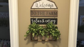 A wall with a welcome sign, a shelf with plants, and a dairy sign. - Charming Cottage by the Lake! (Salt Springs)