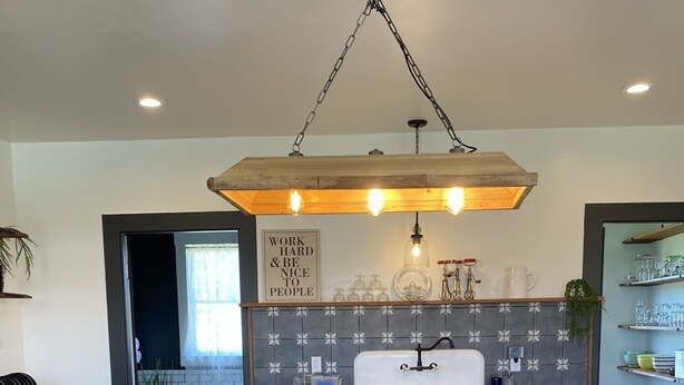 A kitchen with a central island, black barstools, a hanging light fixture, and a backsplash with a floral pattern. - The Red Farmhouse (Ferndale)