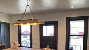 A spacious kitchen with a wooden table, pendant lighting, and large windows. - The Red Farmhouse (Ferndale)