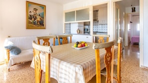 Un'area pranzo con tavolo apparecchiato per quattro persone, una poltrona e una cucina sullo sfondo.