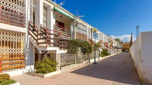 Una fila di edifici in stile mediterraneo con balconi, una strada pavimentata e un cielo azzurro limpido.