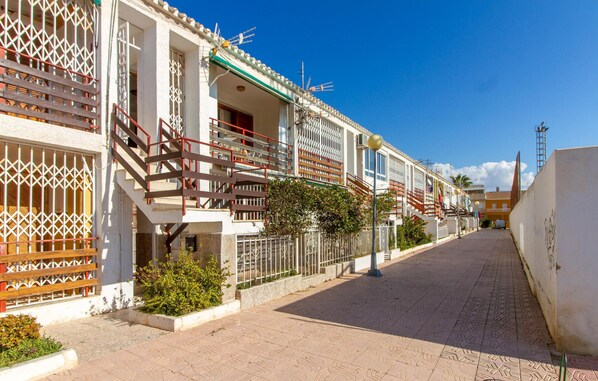 A row of traditional Mediterranean-style buildings with balconies, a paved street, and a clear blue sky. - Beach front apartment in Puerto de Mazarrón (Puerto de Mazarrón)