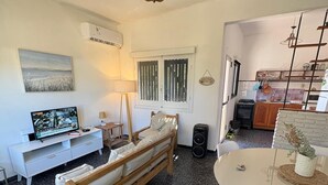 Un espacio habitable compacto con sofá, mesa de comedor, televisor y zona de cocina.
