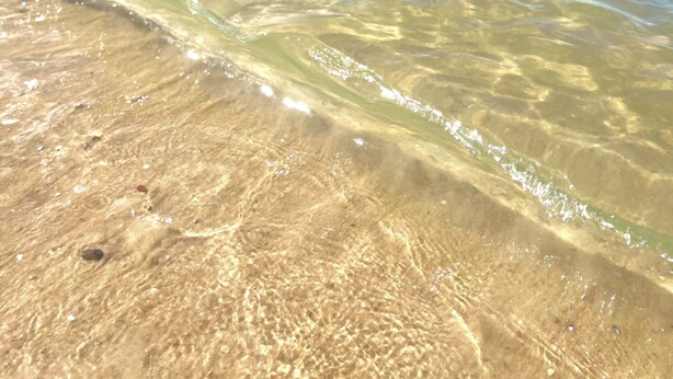 Una playa con agua clara y poco profunda, y una tierra firme a lo lejos.