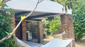 Un espacio al aire libre cubierto con una hamaca, pilares de ladrillo y techo de metal.