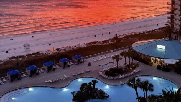 Un resort con zona de piscina, acceso a la playa y vistas al atardecer sobre el océano.