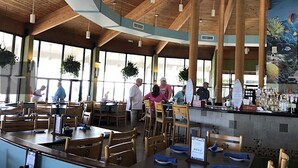 Un restaurante espacioso con altos techos de madera, amplias ventanas y una zona de bar.