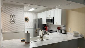 Una cocina moderna con armarios blancos, electrodomésticos de acero inoxidable, encimera de mármol y una barra con taburetes.