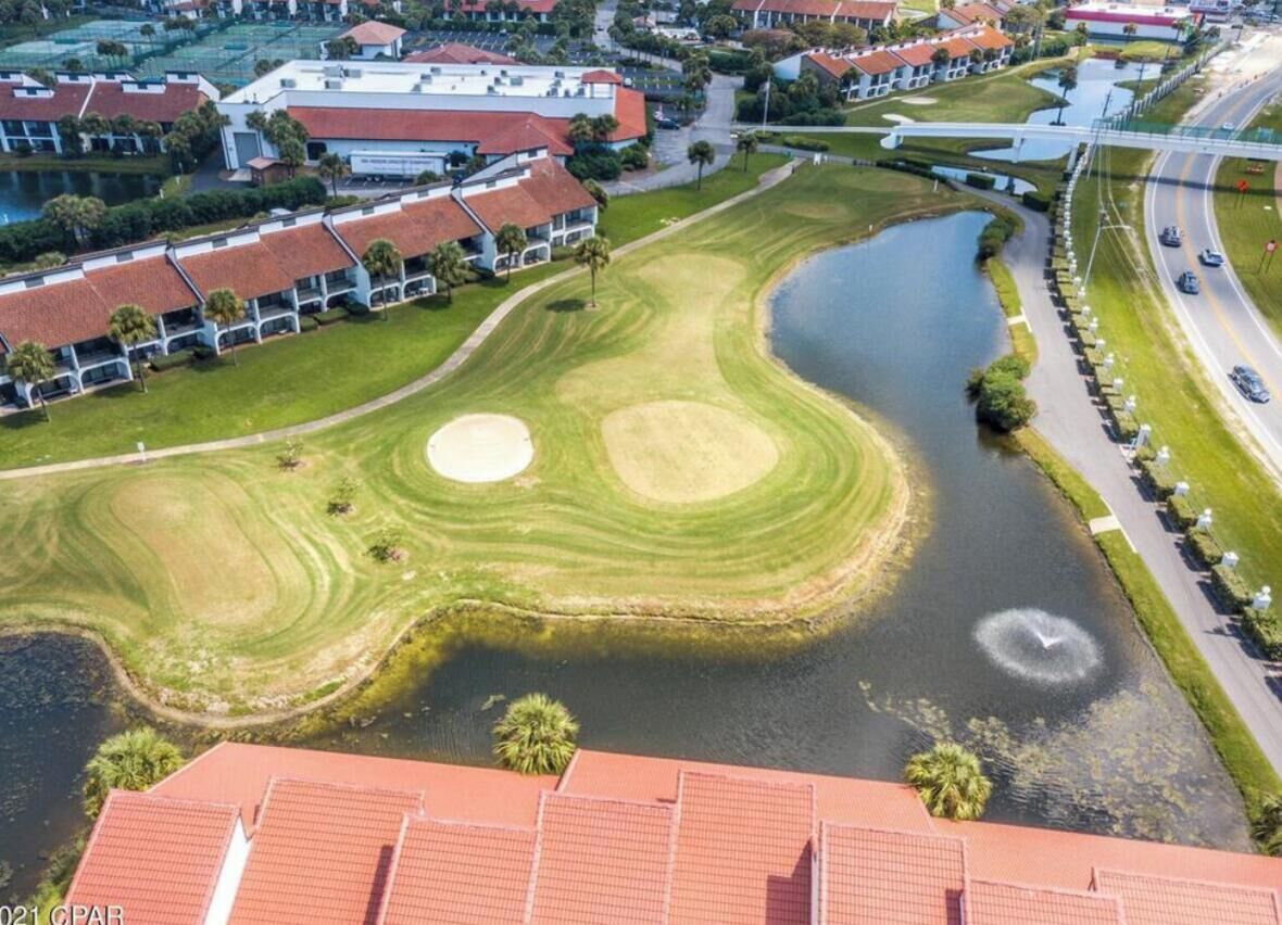 Luftaufnahme eines Golfplatzes mit Teich, umgeben von Wohnhäusern und einer Brücke.