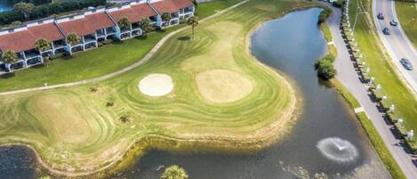 Luftaufnahme eines Golfplatzes mit Teich, umgeben von Wohnhäusern und einer Brücke.