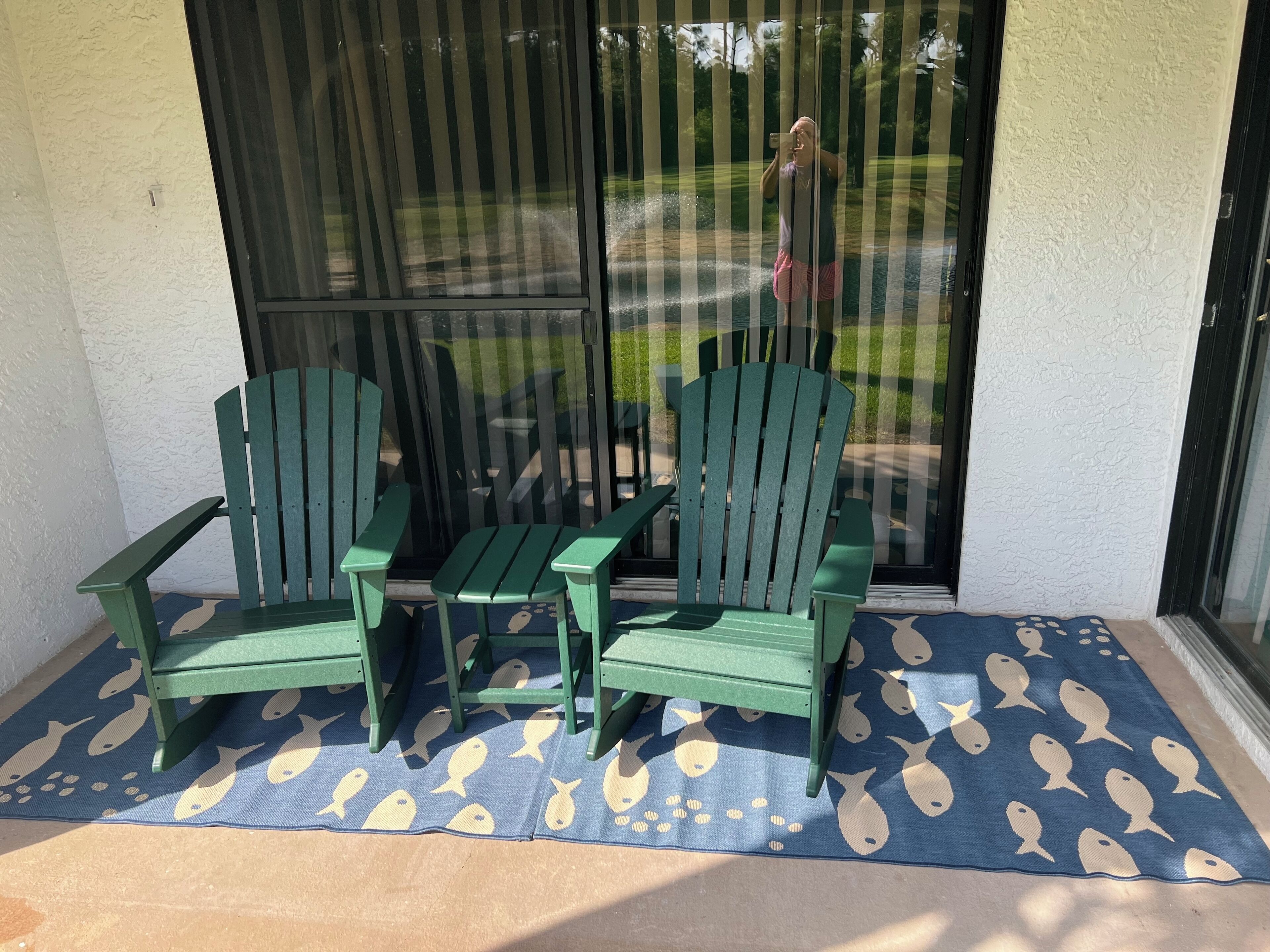 A patio area with two green Adirondack chairs and a small table, covered by a blue mat with fish patterns.