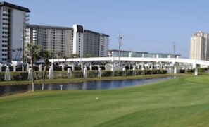 Campo de golf con un puente, un cuerpo de agua y edificios al fondo.