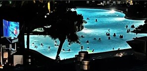 Guests can enjoy a refreshing swim under the stars at our pool, surrounded by a shaded area and a large screen displaying entertainment.