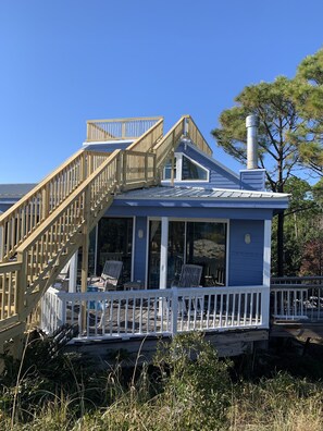 Uma casa à beira-mar com um deck de madeira, escadas e uma chaminé.