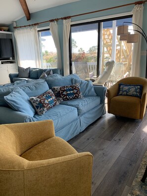 Uma sala de estar com um sofá azul, uma poltrona mostarda e piso de madeira.