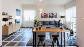 A modern living space with a wooden dining table, two black stools, a grey sofa, and a blue door.