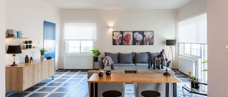 A modern living space with a wooden dining table, two black stools, a grey sofa, and a blue door.