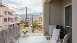 A balcony with a table and chairs, a potted plant, and a view of buildings and mountains in the background.