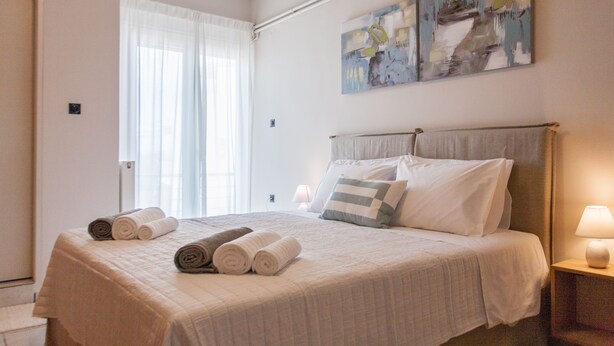 A neatly made bed with rolled towels, a bedside lamp, and abstract wall art.