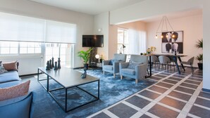 A modern living room with a sofa, a coffee table, and a dining area with chairs and a table.