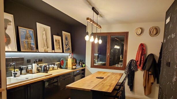 A modern kitchen with a wooden island, dark cabinetry, and a large window. - Cozy attic apartment (Charmes-sur-Rhône)