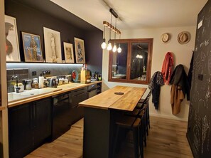 A modern kitchen with a wooden island, dark cabinetry, and a large window.
