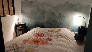 A bedroom with a bed, a nightstand, a desk, and a wall with a painting. - Cozy attic apartment (Charmes-sur-Rhône)