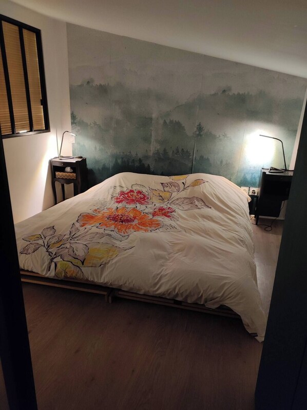 A bedroom with a bed, a nightstand, a desk, and a wall with a painting.