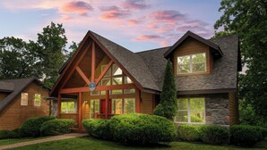 A modern house with a prominent gable roof, large windows, and a stone exterior.