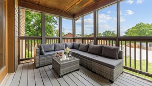 A covered porch with wicker furniture, a glass coffee table, and a view of the neighborhood.