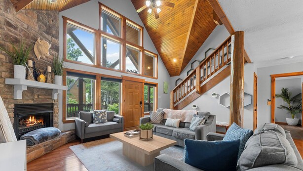 A spacious living room with a fireplace, large windows, and a wooden ceiling.