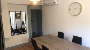 Un espace de salle à manger moderne avec une table en bois, des chaises noires, un luminaire suspendu et une horloge fixée au mur.