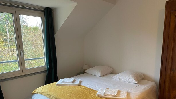Un lit simple avec une couvre-lit jaune à motifs, des oreillers blancs et deux serviettes pliées posées sur le lit.
