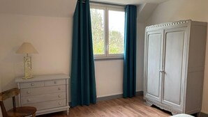 Une chambre à coucher comprenant un lit, une commode, une chaise, une armoire et une fenêtre avec des rideaux.