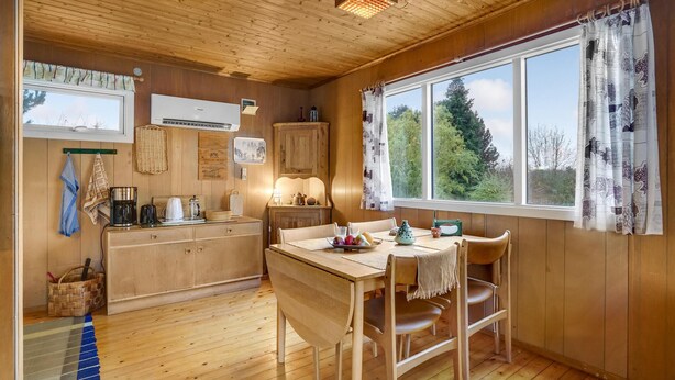A wooden interior with a dining table, chairs, a kitchen area with a coffee maker, and a window with curtains. - Nice home in Holbæk with kitchen (Holbæk)