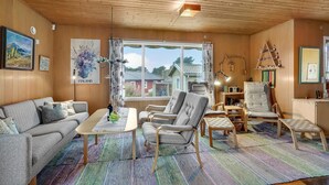 A cozy living room with a wooden ceiling, a large window with curtains, a sofa, two armchairs, a small table with a bottle and glasses, and a radio. - Nice home in Holbæk with kitchen (Holbæk)