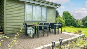 A patio with a table and chairs, a window, and a garden with flowers and a lawn. - Nice home in Holbæk with kitchen (Holbæk)