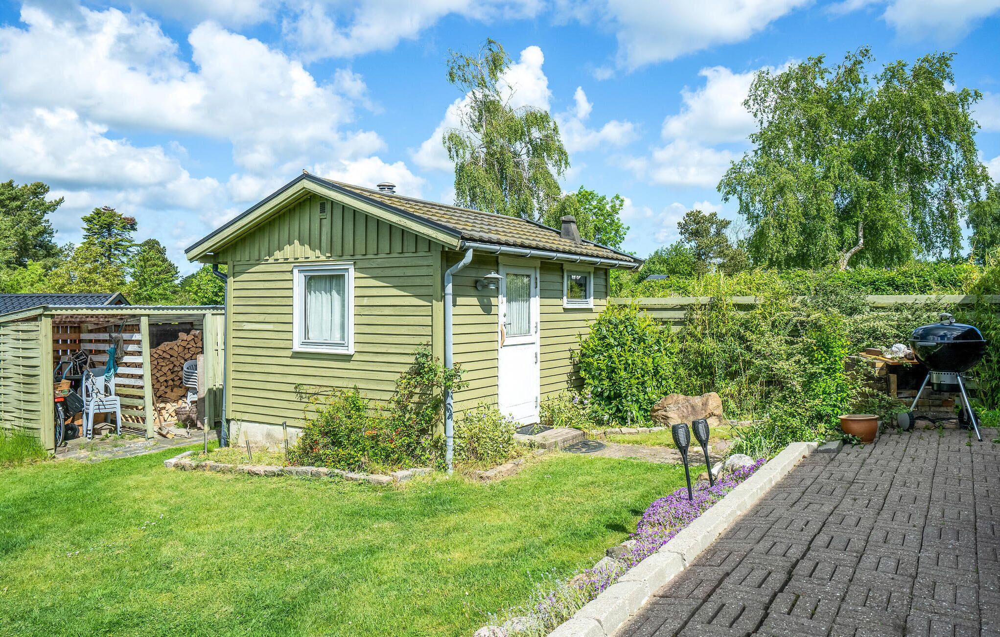 A small house with a front yard, a wooden shed, and a barbecue grill.