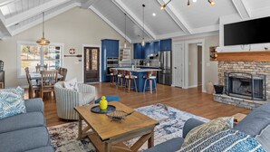 Amplia sala de estar con techos altos, chimenea, cocina con armarios azules y comedor con mesa y sillas.
