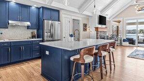 Una cocina moderna con armarios azul oscuro, una isla grande con taburetes de bar, electrodomésticos de acero inoxidable y una chimenea de piedra.