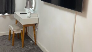A room with a white desk, a vanity with a mirror, a grey carpet, and a flat-screen TV mounted on the wall. - Affordable luxury apartment (Stratford)