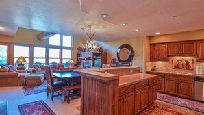 A spacious kitchen with wooden cabinets, a central island, and a dining area with a table and chairs. - Spacious Mtn Retreat - 3 Minute Walk to Slopes + Hot Tub & Garage (Crested Butte)