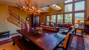 A spacious living room with a large wooden dining table, comfortable seating, and a rustic chandelier. - Spacious Mtn Retreat - 3 Minute Walk to Slopes + Hot Tub & Garage (Crested Butte)