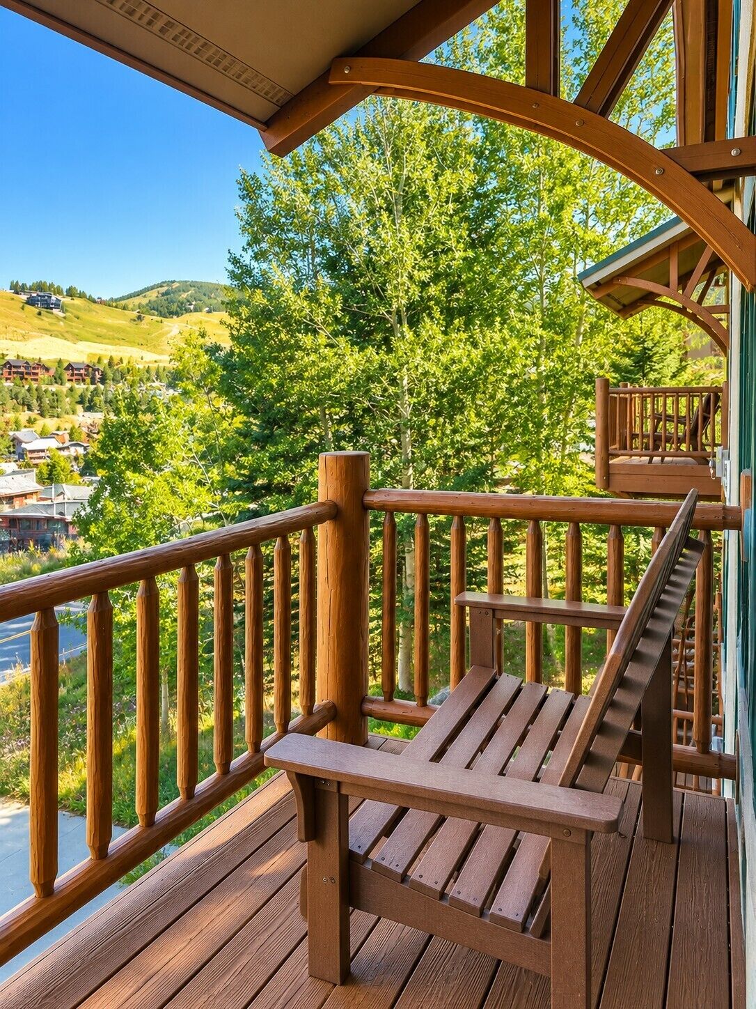 A wooden deck with a bench and railing overlooking a scenic landscape with trees and buildings.