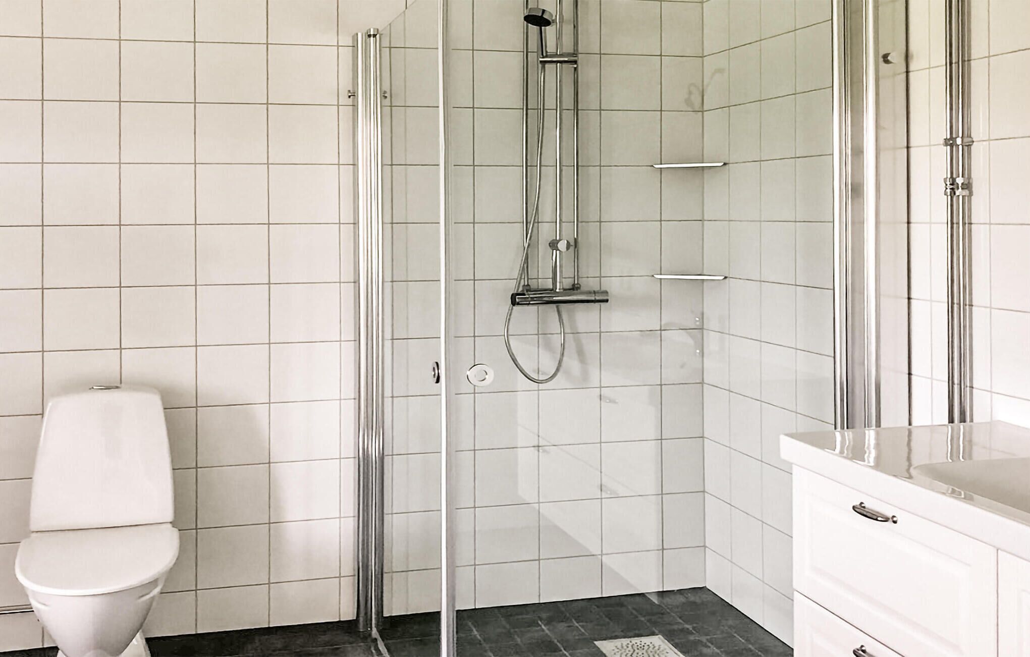 A modern bathroom with a glass-enclosed shower, a white toilet, and a white vanity with a mirror.