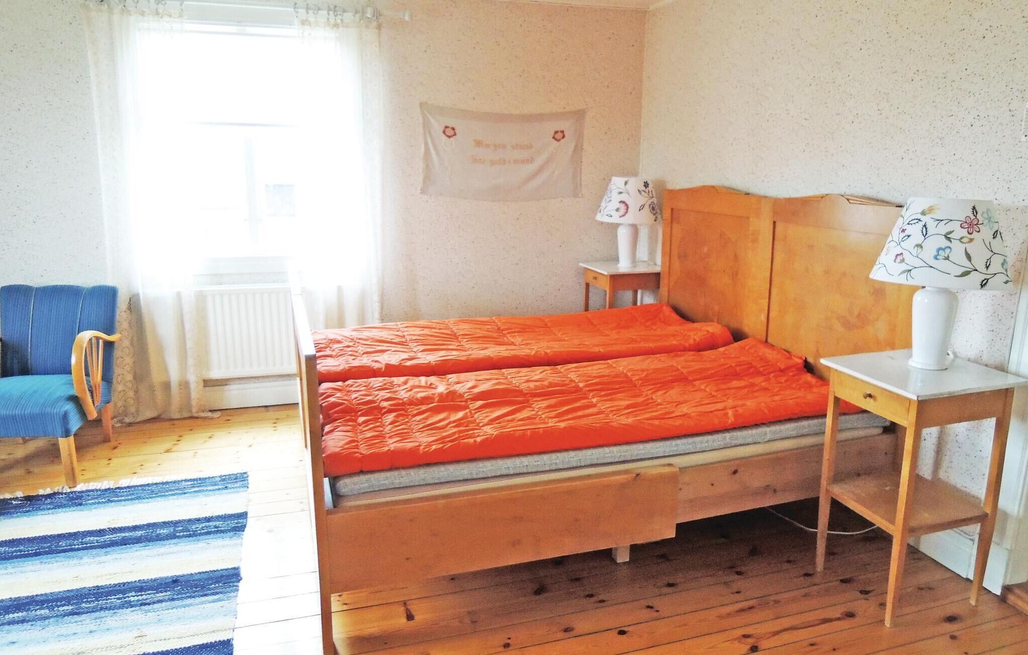 A bedroom with a wooden bed, a blue chair, a radiator, a window with curtains, and a wall with a sign.