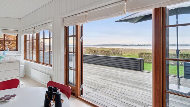 A room with large windows, a wooden deck, and a view of a lake. - 2 bedroom awesome home in Holbæk (Holbæk)