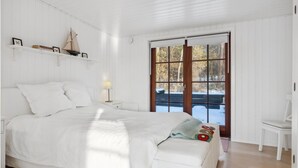 A bedroom with a large bed, a nightstand with a lamp, a window with a view of a snowy landscape, and a small chair. - 2 bedroom awesome home in Holbæk (Holbæk)